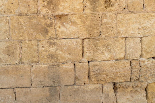 Beige limestone brick wall with rough weathered blocks and thin mortar joints filling the frame, close-up of old sandstone masonry in a historic Italian town, natural stone texture background, concep