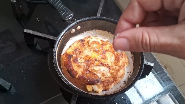 Hand seasoning fried egg in metal pan