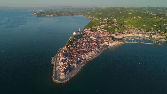Panoramic drone flying sideways over the Adriatic Sea, revealing Piran waterfront, lighthouse and coastal landscape.
