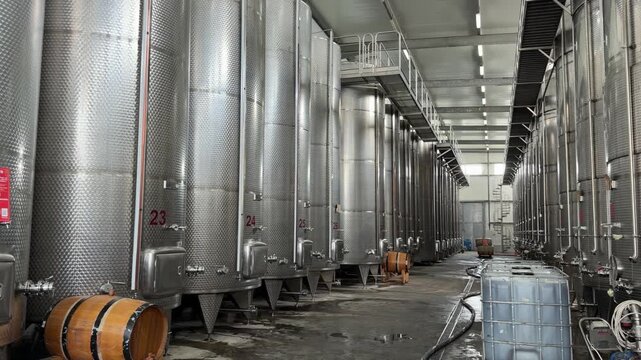 factory, Georgia - September 03, 2026: Stainless steel fermentation tanks are lined up in a winery facility with wooden barrels and industrial equipment present