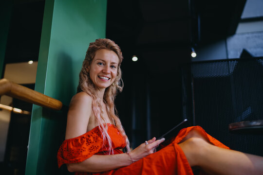 Confident Caucasian female student looking at camera while holding tablet for online education course, authentic representation of happy freelancer enjoying digital nomad lifestyle