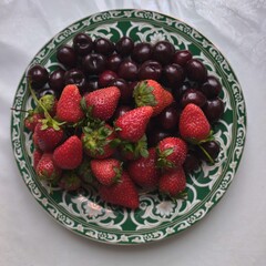 Fresh strawberries and dark cherries arranged on a decorative patterned plate © IMRAN_IM33