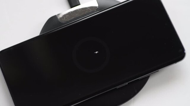 A hand placing a smart phone onto a wireless charger to charge the device. A technology, energy use concept.