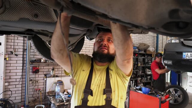 Skilled mechanic in brown overalls works diligently under vehicle, utilizing tools to perform repairs, showcasing the intricate process of automotive maintenance and expertise in a garage environment