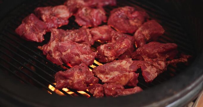 A man puts pieces of raw meat on the grill of a round grill, hot coals under the grill, and an egg-shaped grill.