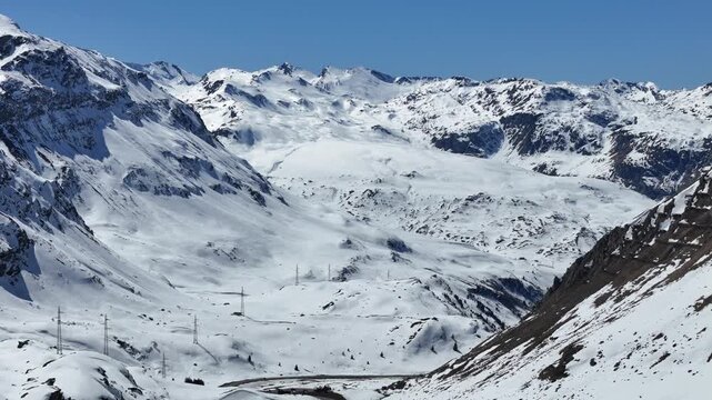 wide snowfield basin spreads beneath distant mountain ridge scattered pylons trace faint road below julier pass alpine terrain graubunden switzerland high altitude european alps