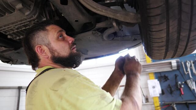 Skilled mechanic working under a vehicle, using a power tool to remove components, showcasing the intricate process of automotive repair in a well-equipped garage environment