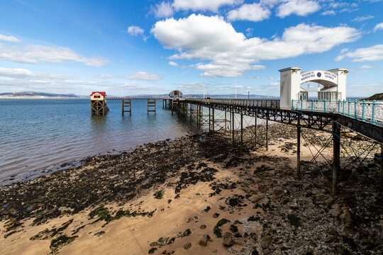 Mumbles Pier structure extending over the rocky beach and sea under a cloudy blue sky in Swansea Wales