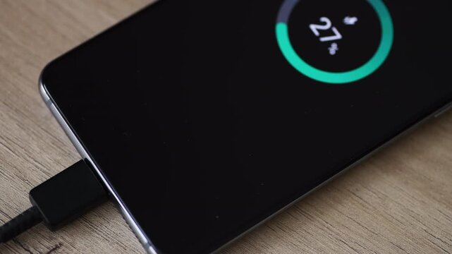 A hand plugging a power cable into a mobile phone USB port to charge the device. A technology, electricity use concept.