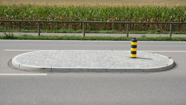 Verkehrsinsel und Leitpfosten zur Verkehrsberuhigung auf einer Landstra&szlig;e im Sommer