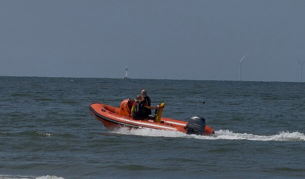 den haag, netherlands - July 25 2026: two men aboard an orange rigid inflatable boat on the North Sea off den haag coast with wind turbines on the horizon