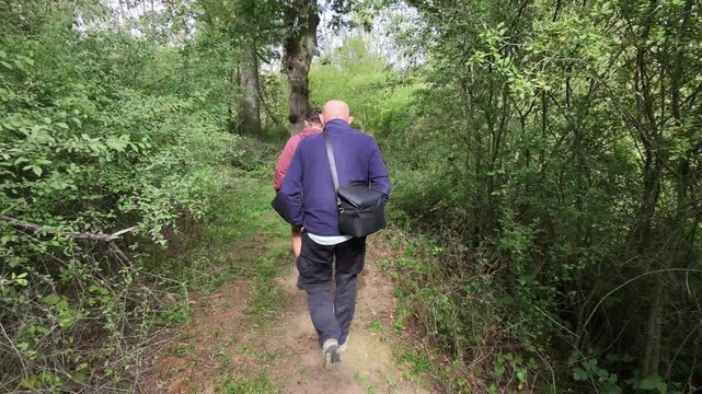 Two people walk along a narrow forest path