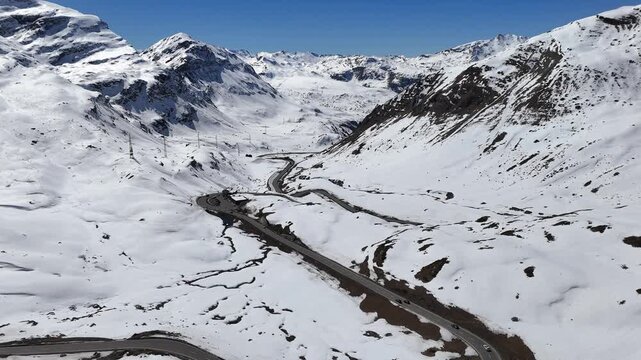 serpentine switchback complex loops past snowbound rest stop cars trace hairpin bends down mountainside power lines cross ridge above julier pass mountain crossing graubunden switzerland high altitude
