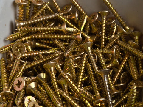 Gold Zinc Wood Screws Pile Close-Up - Large pile of gold zinc-plated countersunk Phillips head wood screws filling a storage bin, macro detail view.
