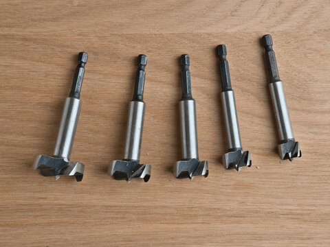 Five Forstner Drill Bits on Wood Surface - Set of five steel Forstner drill bits arranged on a light oak wooden surface, varying sizes for woodworking.