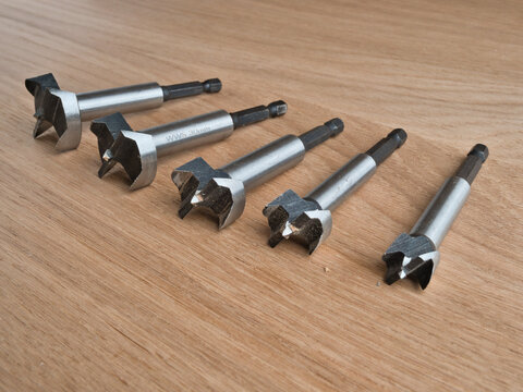 Five Forstner Drill Bits on Wood Surface - Set of five steel Forstner drill bits arranged on a light oak wooden surface, varying sizes for woodworking.