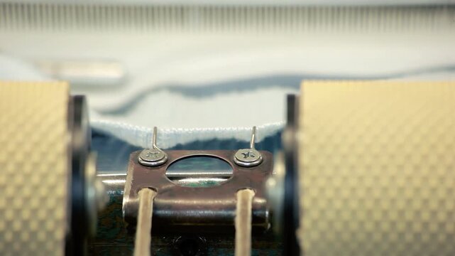 Knitting machine macro. Textile factory equipment feeding white knitted fabric.