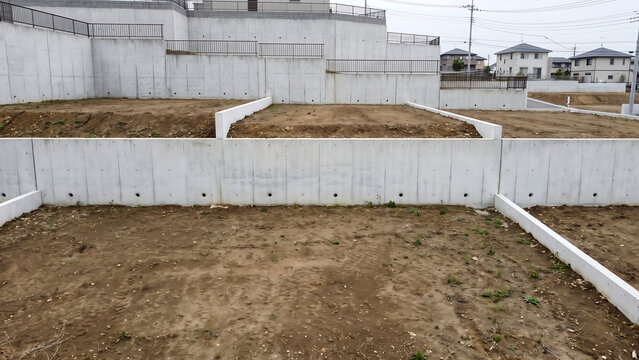 段差のある造成地で水抜き穴と区画境界が見えるコンクリート擁壁を戸建て住宅とともに捉えた開発風景