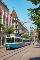Fototapeta premium ZURICH, SWITZERLAND - JUNE 28, 2026: Blue public tram line 7 driving past historic buildings on Bahnhofstrasse in Zurich city center