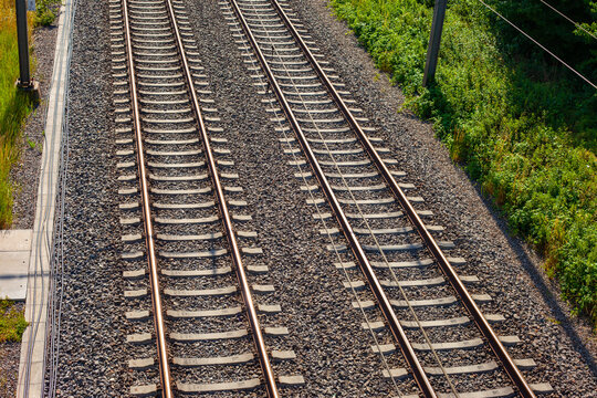 High angle view of parallel railway tracks on gravel ballast with green vegetation and copy space