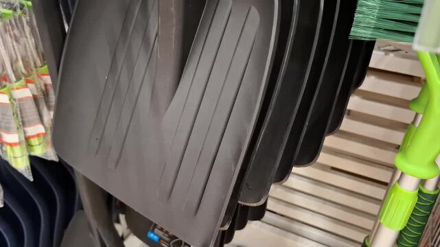Row of black plastic snow shovels on a store display shelf, winter season preparation and household cleaning tools retail concept.