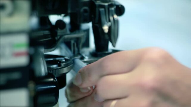 Tailor hands feeding fabric industrial sewing machine. Close up garment factory.