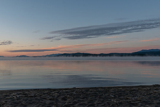 Pink orange sunrise over calm lake with mountains in background