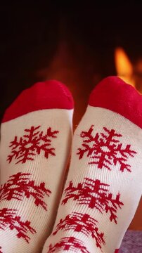 Feet dressed in wool socks with a Christmas ornament in front of the fireplace. The person is having fun at home on Christmas Eve. Vertical video