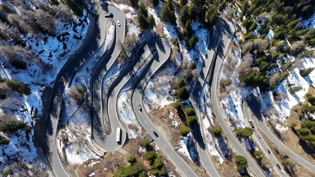 switchback road coils through pine forest bus truck cars wind past stacked hairpin bends snow patches maloja pass aerial drone footage graubunden switzerland