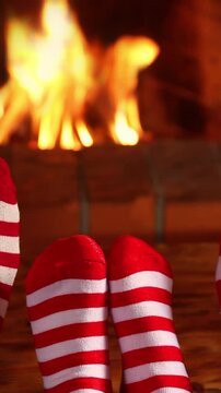 Feet dressed in wool socks with a Christmas ornament in front of the fireplace. Vertical video