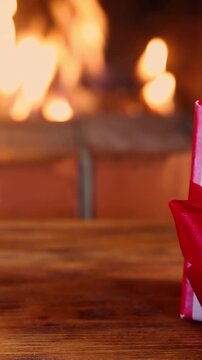 Mugs in knitted woolen covers with a Christmas ornament are placed in front of the fireplace. Xmas decorations on a wooden table in front of a flame burning in the fireplace. Vertical video