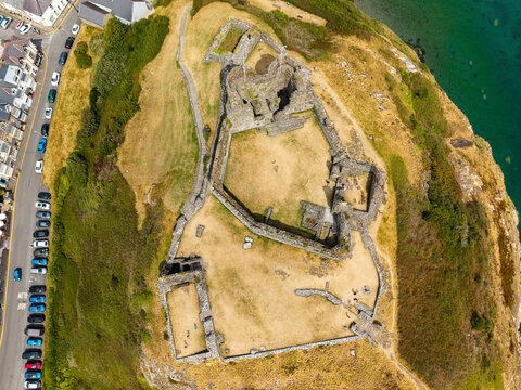 Aerial top down view of ruined stone castle walls on dry grassy hill, historic stronghold built on strategic headland, Wales, UK