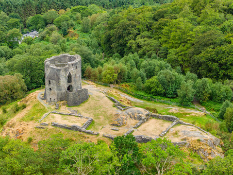Medieval round stone keep and castle ruins standing on grassy hill, dense forest canopy extending behind historical landmark in Eryri