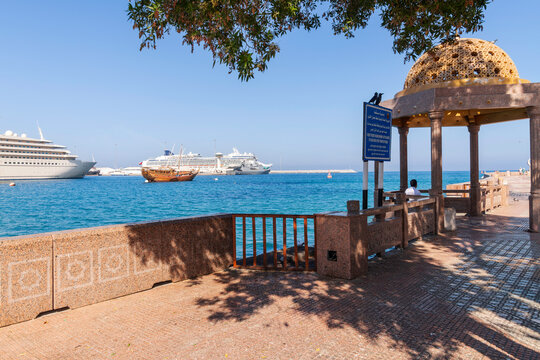 A decorative stone gazebo sun shelter along the Mutrah Corniche waterfront promenade in Muscat, Oman with traditional wooden dhows, cruise ships and yachts in the harbor.