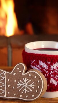 Mugs in knitted woolen covers with a Christmas ornament are placed in front of the fireplace. Xmas decorations on a wooden table in front of a flame burning in the fireplace. Vertical video