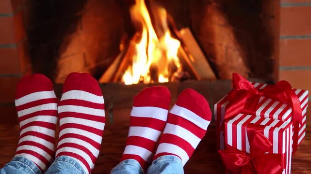 Feet dressed in wool socks with a Christmas ornament in front of the fireplace. The couple is having fun at home on Christmas Eve