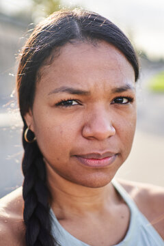 Confident. Close-up portrait of an African millennial woman standing outdoors in park after exercise, wearing sportswear and looking at camera. Natural light portrait shows strength active lifestyle