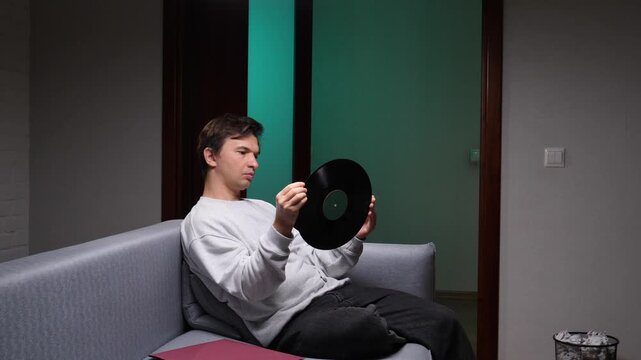 Man relaxing on sofa at home holding a vintage vinyl record, lost in music and nostalgia, enjoying analog sound, quiet weekend leisure and thoughtful, collectible album appreciation