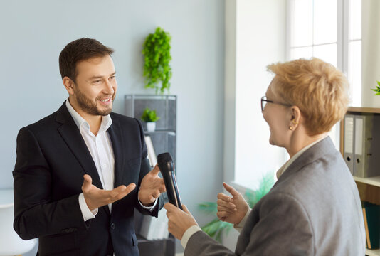 Business interview as reporter hands microphone to speaker. A confident executive gestures in a bright office, showing media communication. Woman journalist interviewing man. Journalism.