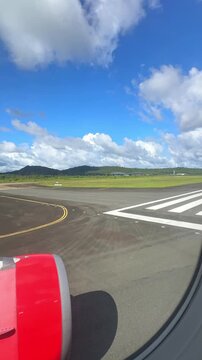 Airplane wing view from runway with green landscape and mountains under a blue sky with clouds, showcasing aviation and travel experience. 4K vertical footage