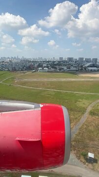 Airplane wing and engine view during landing approach over green grass runway with city skyline and clouds in the background. 4K vertical footage