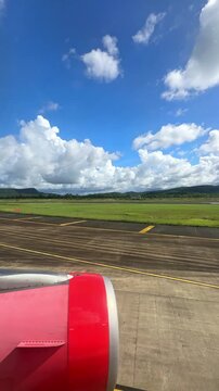 Airplane wing and engine view from window overlooking green landscape and blue sky with fluffy clouds during daytime flight. 4K vertical footage
