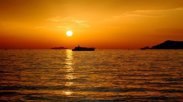 Silhouette of a passenger ferry navigating the Marmara Sea at sunset, with a vibrant golden sun reflecting on rippled water and the Princes' Islands in the background. Istanbul, Turkey.