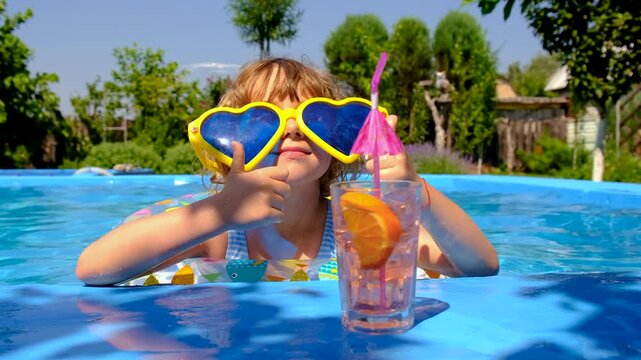 A child is drinking a cocktail by the pool. Selective focus.