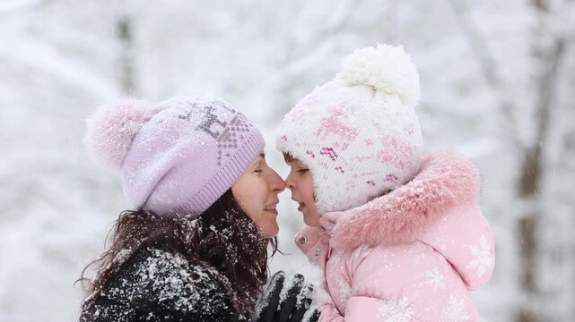 Mother and child are having fun outdoors in winter forest. A family plays in a nature park against a snow covered trees background. Healthy lifestyle and winter holidays concept.