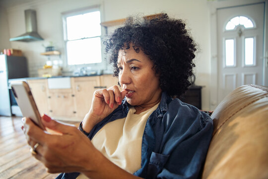 Worried woman biting her nail while reading smartphone at home