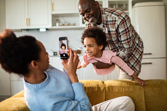 Woman photographing playful child while man holds her at home