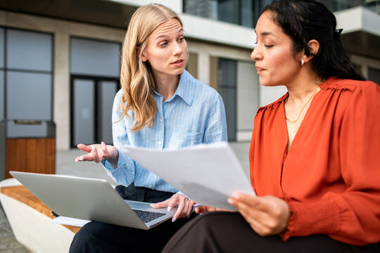 Two coworkers reviewing documents with a laptop outside the office
