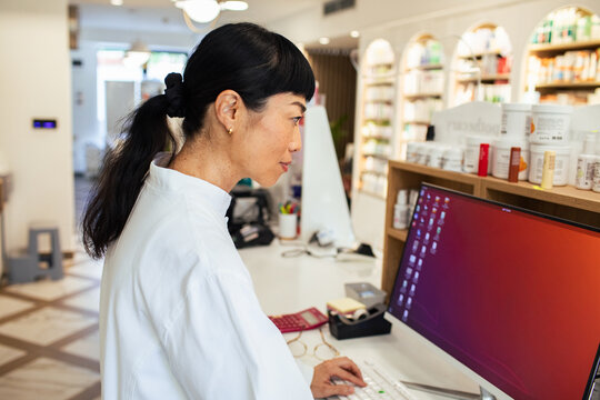 Female pharmacist using computer at pharmacy counter