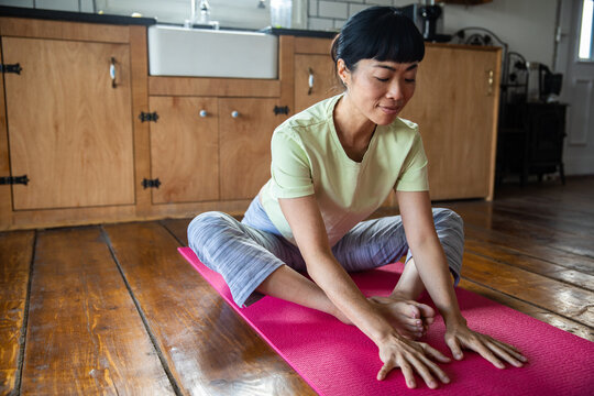 Woman practicing yoga stretch on pink mat in home kitchen